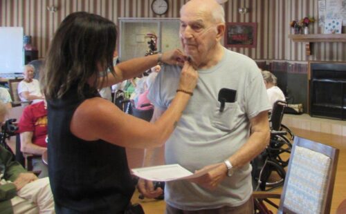 A woman attaches a pin to a Veteran's collar.