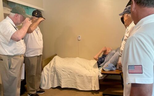 Four veterans salute a veteran lying in bed.