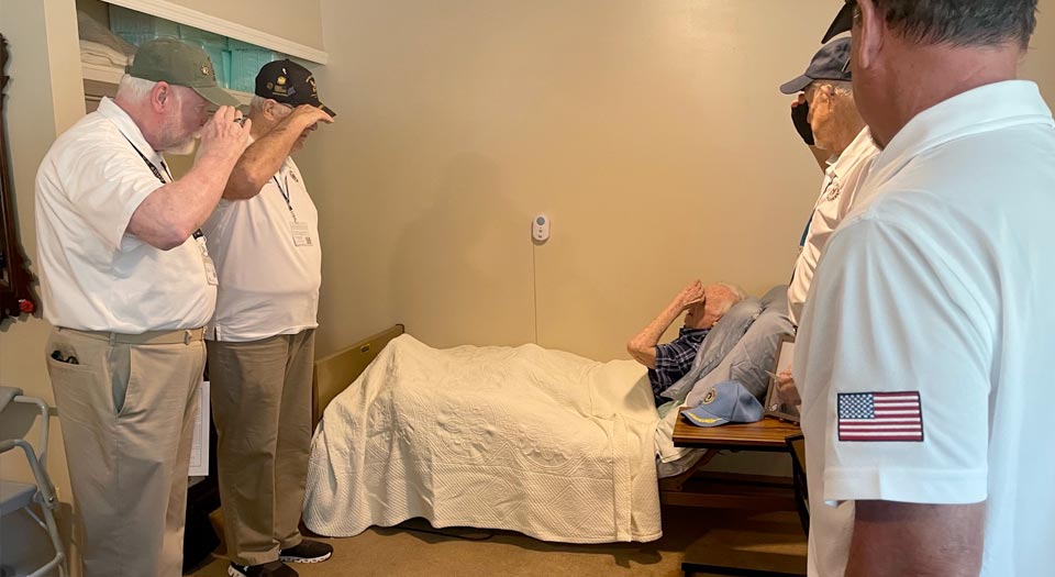 Four veterans salute a veteran lying in bed.